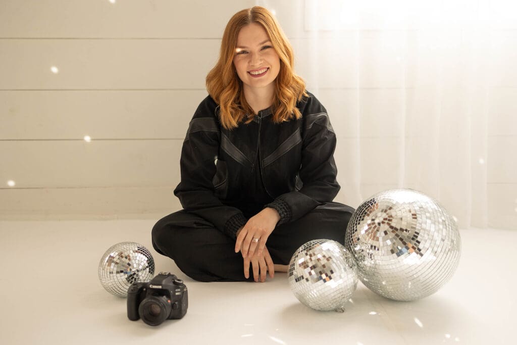 Woman sitting criss cross applesauce wearing all black surrounded by disco balls.